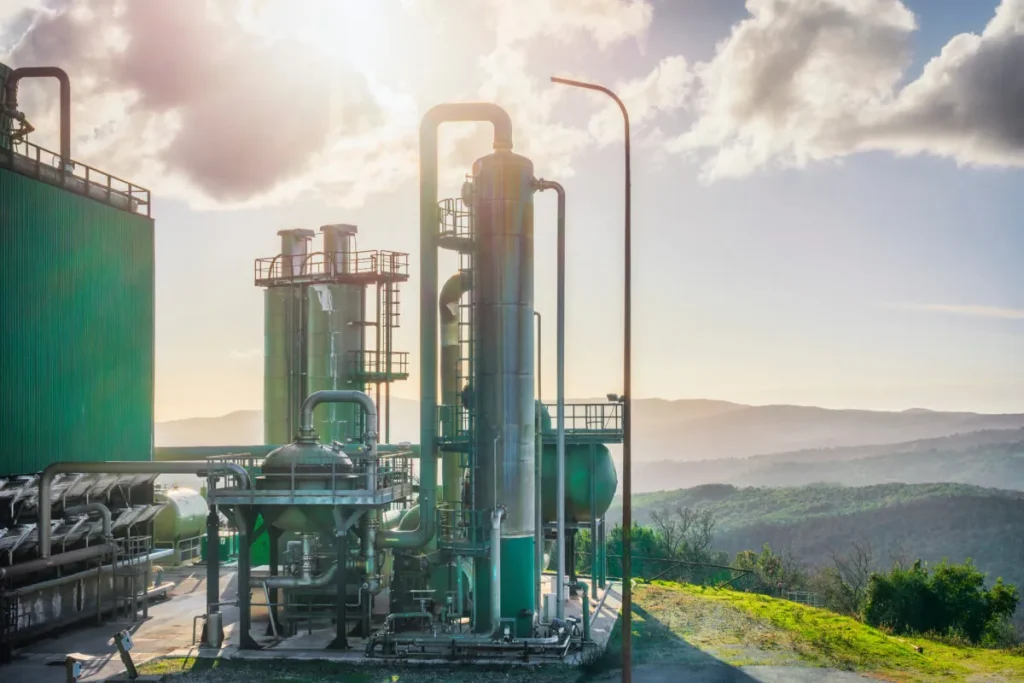 Geothermal industrial facility with green metal piping, towering steel equipment and steam rising under a dramatic sky for high-temperature, high-pressure wells