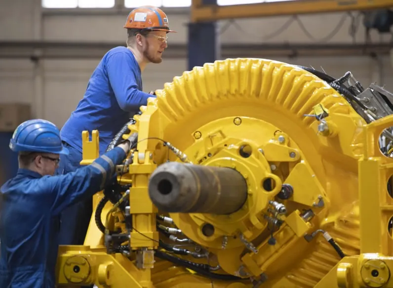 API-certified workshop scene with yellow drilling equipment and blue-clad team members wearing hard hats while performing training and knowledge transfer work.